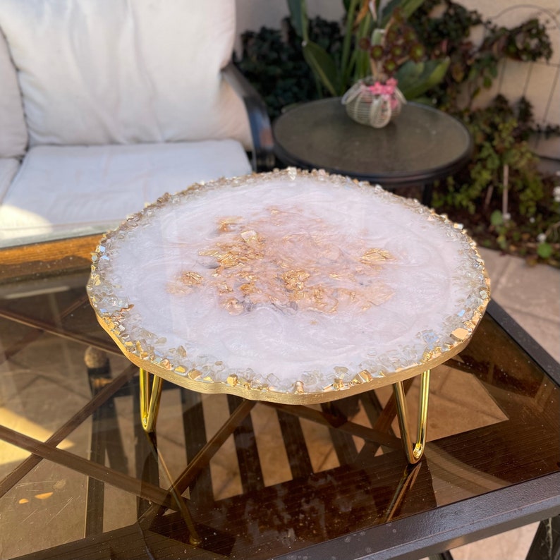 May include: White resin serving tray with gold flecks and a gold metal stand. The tray is decorated with clear crystals around the edge.