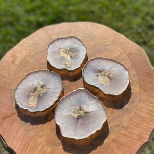 May include: Four round, light purple coasters with gold flecks. The coasters have a slightly wavy edge and are arranged in a circle on a wooden surface.