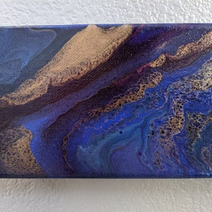 Puede incluir: Pintura abstracta sobre lienzo con remolinos azules, dorados y morados. La pintura tiene una superficie texturizada y un estilo moderno.