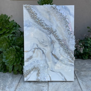 May include: White canvas painting with a gray marble design and silver glitter accents. The painting has a textured, raised surface.