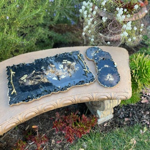 May include: A black and gold resin serving tray with a wavy edge and a gold handle. Four matching black and gold resin coasters are included.