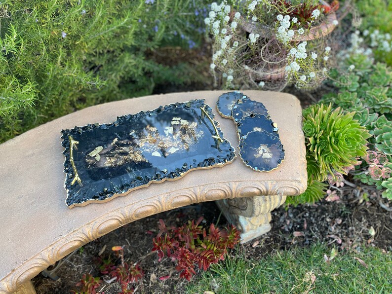 May include: A black and gold resin serving tray with a wavy edge and a gold handle. Four matching black and gold resin coasters are included.