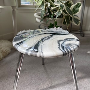 May include: A small, round, white and black marble table with a glossy finish. The table has three silver legs.