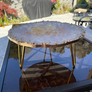 May include: A round, white agate slice table top with gold accents and a gold metal stand with three legs.