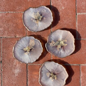 May include: Set of four round, white resin coasters with gold flecks and a slightly irregular, organic shape. The coasters are arranged on a brick surface.