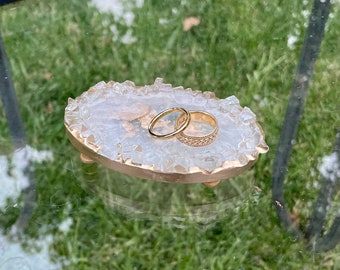 May include: A white agate ring holder with two gold rings on top. The holder is made of clear agate with a gold rim and has a rough, textured surface.