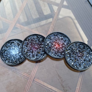 May include: Four black coasters with a glittery, speckled surface. The coasters have a variety of colors, including black, red, and white.