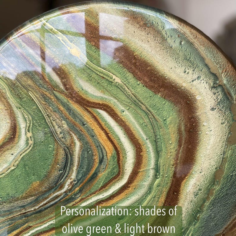 Op de afbeelding: Close-up van een ronde, kunsthars onderzetter met een draaiende patroon van olijfgroen en lichtbruine kleuren. Personalisatie: tinten van olijfgroen en lichtbruin