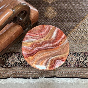 May include: A round side table featuring a glossy resin tabletop with a swirling, marbled pattern in shades of deep red, burnt orange, metallic gold, and white, creating a fluid, multi-layered appearance across the circular surface.