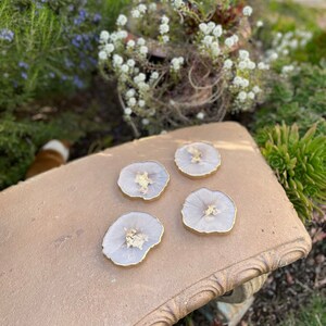 May include: Four round, white, resin coasters with gold flecks. The coasters are on a brown, textured surface.