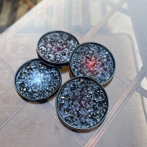 May include: Four black coasters with a glittery finish. Each coaster has a different color of glitter embedded in the resin, including red, blue, and black.