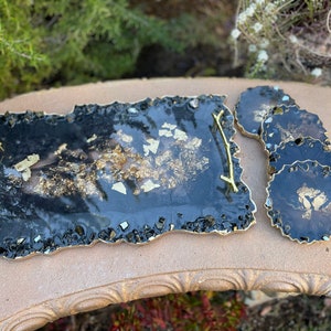 May include: A black and gold resin serving tray with a gold handle and four matching coasters. The tray and coasters have a unique, irregular shape and are decorated with gold flakes.