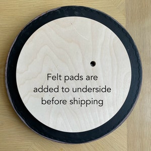 Op de afbeelding: Een ronde houten draaitafel met een zwarte rand. De tekst "Felt pads are added to underside before shipping" is op het oppervlak gedrukt.