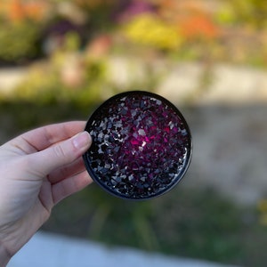 May include: A round black coaster with a pink and black glitter design.