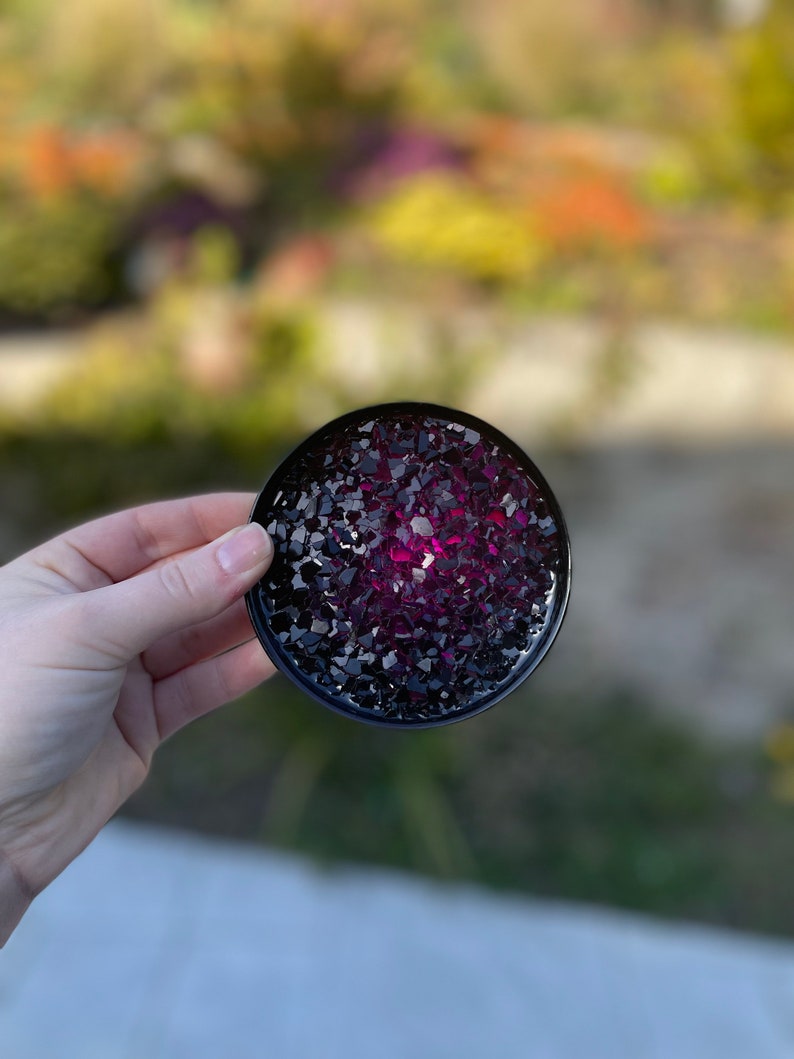 May include: A round black coaster with a pink and black glitter design.