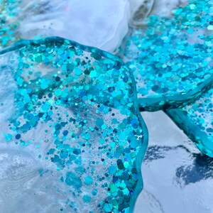May include: Close-up of a set of blue and white resin coasters with a glittery finish. The coasters are shaped like irregular circles and have a translucent appearance.