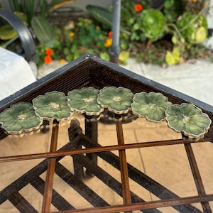 Peut inclure: Six sous-verres en r&eacute;sine verte et dor&eacute;e avec un motif floral. Les sous-verres sont dispos&eacute;s en rang&eacute;e sur une table en verre.