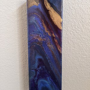 Puede incluir: Pintura abstracta sobre lienzo con colores azules, morados y dorados en espiral. La pintura tiene una superficie texturizada y un estilo moderno.