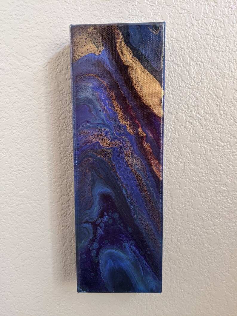 Puede incluir: Pintura abstracta sobre lienzo con colores azules, morados y dorados en espiral. La pintura tiene una superficie texturizada y un estilo moderno.