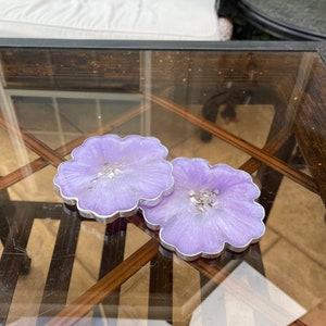 Op de afbeelding: Twee paarse onderzetters van hars met een zilveren glitteraccent. De onderzetters zijn bloemvormig en hebben een zilveren rand.