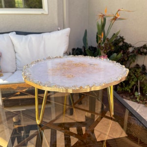 May include: A white resin cake stand with gold flecks and a gold metal base. The stand has a unique, irregular shape and is perfect for displaying cakes, desserts, or other treats.