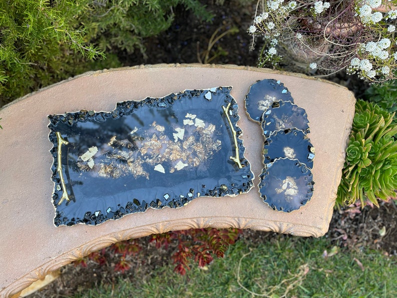 May include: A black resin serving tray with gold flecks and a gold handle. Four black coasters with gold flecks are also included.