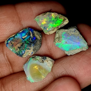 Op de afbeelding: Vier ruwe opaal edelstenen in verschillende kleuren, waaronder groen, blauw en wit. De opalen zijn gezet in een ruwe, natuurlijke matrix.