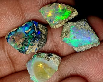 May include: Four rough opal gemstones with a variety of colors, including green, blue, and white. The opals are set in a rough, natural matrix.