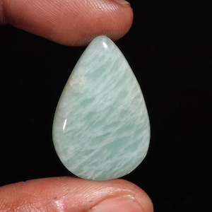 May include: A polished, teardrop-shaped gemstone featuring a smooth surface with a pale mint green colour and white, cloud-like marbled patterns throughout. The stone has a glossy finish and a rounded, symmetrical form, displaying natural mineral variations.