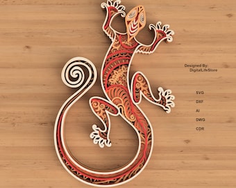 May include: An intricate laser cut design of a gecko lizard with a swirling tail. The gecko is in shades of red, orange, and brown with white accents. The design is on a wood background.