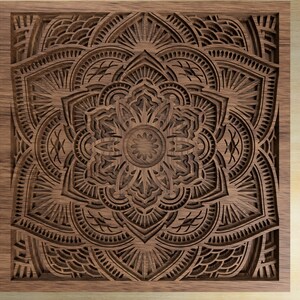 Op de afbeelding: Een gedetailleerd mandala-ontwerp dat in een stuk hout is gegraveerd. De mandala is ingewikkeld en symmetrisch, met een verscheidenheid aan vormen en patronen. Het hout is een rijke bruine kleur, en de gravure is zeer precies.