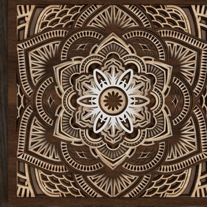 Op de afbeelding: Een lasergesneden mandala-ontwerp met ingewikkelde details in bruin en wit. Het ontwerp is ingelijst in een donkerhouten lijst.