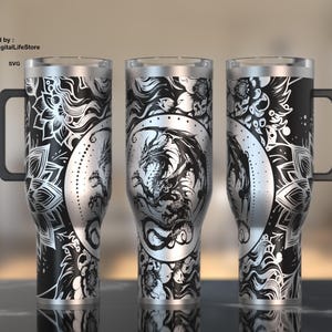 Puede incluir: Un vaso de acero inoxidable plateado con un diseño en blanco y negro que presenta un dragón y patrones florales. El vaso tiene un asa y está diseñado para bebidas calientes o frías.
