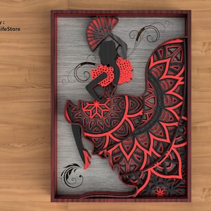 Op de afbeelding: Een gelaagd papier snijontwerp in rood en zwart van een vrouw in een flamencojurk met een waaier. Het ontwerp is ingelijst in een rood houten frame.