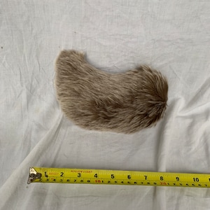 Puede incluir: Una pieza de piel marrón claro con forma curva, que mide aproximadamente 25 cm de largo.