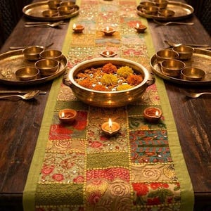 May include: A long rectangular table runner featuring a patchwork of colorful floral fabrics with green borders and tassels, set on a wooden table with brass plates, small bowls, a large central brass bowl filled with flowers, and lit clay oil lamps.