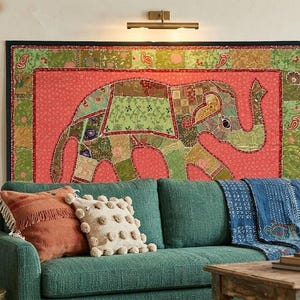 May include: A rectangular wall hanging featuring a patchwork elephant design in shades of green and gold against a coral background, framed in black. The elephant is composed of various patterned fabric segments with decorative stitching.