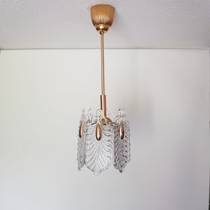 May include: A gold and clear glass chandelier with a geometric design. The chandelier has a round, gold-colored ceiling mount and hangs from a single chain.