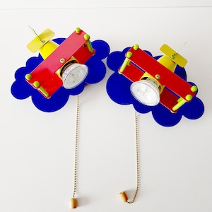 May include: Two red and yellow aeroplane-shaped ceiling lights with blue cloud-shaped bases. Each light has a pull chain and a white light bulb.