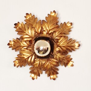 Könnte beinhalten: Goldfarbene Wandleuchte mit einem zentralen Spiegelkugel, umgeben von aufwendigen, blattförmigen Details. Die Leuchte hat ein symmetrisches, florales Design und ist wahrscheinlich aus Metall. Die Gesamtästhetik ist Vintage oder antik.