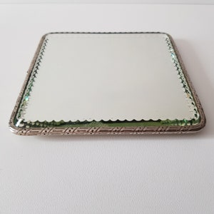 Könnte beinhalten: Ein Schminkspiegel mit silbernem Rahmen und einem dekorativen Rand. Der Spiegel hat einen gewellten Rand und eine grüne Tönung.