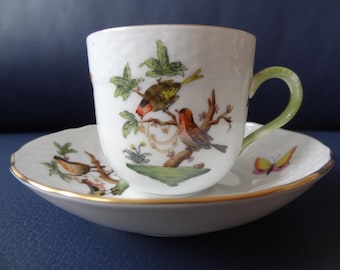May include: A white porcelain teacup and saucer set featuring hand-painted illustrations of birds perched on branches, green leaves, and a small butterfly. The cup has a light green handle, and both pieces are finished with a thin gold rim.