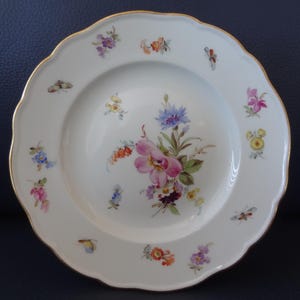 May include: White porcelain plate with a scalloped edge and gold trim. The plate is decorated with colorful floral and butterfly motifs. A large bouquet of pink, purple, and blue flowers is in the center.