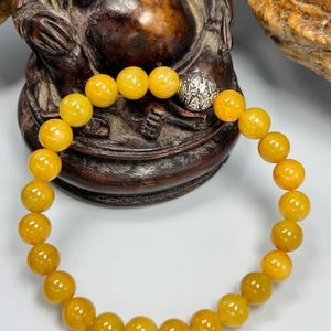 Pode incluir: Uma pulseira de contas com contas redondas de cor &acirc;mbar. As contas t&ecirc;m aproximadamente 0,8 cm de di&acirc;metro. A pulseira inclui uma conta prateada com um design ornamentado. A pulseira &eacute; exibida em um fundo neutro.