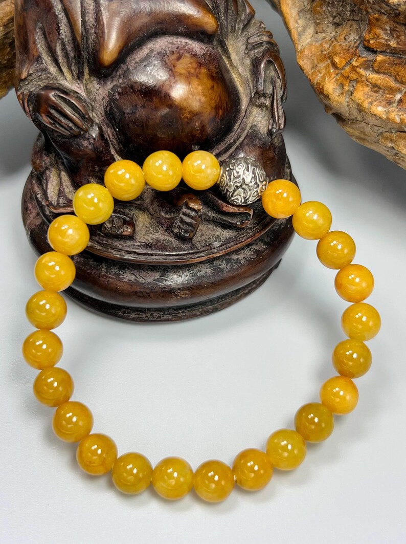 Pode incluir: Uma pulseira de contas com contas redondas de cor &acirc;mbar. As contas t&ecirc;m aproximadamente 0,8 cm de di&acirc;metro. A pulseira inclui uma conta prateada com um design ornamentado. A pulseira &eacute; exibida em um fundo neutro.