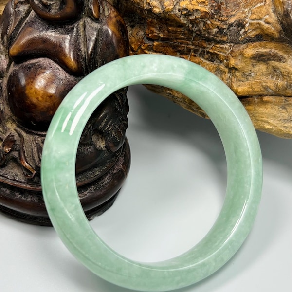 May include: A smooth, polished light green jade bangle bracelet with a rounded profile and a translucent, mottled appearance. The circular band features subtle variations in color intensity, ranging from pale mint to soft sage green throughout.