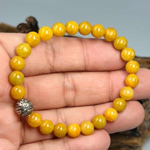 Pode incluir: Uma pulseira de contas redondas amarelas. A pulseira tem uma conta prateada ornamentada. As contas s&atilde;o de uma cor amarela vibrante. A pulseira &eacute; mostrada na m&atilde;o de uma pessoa.