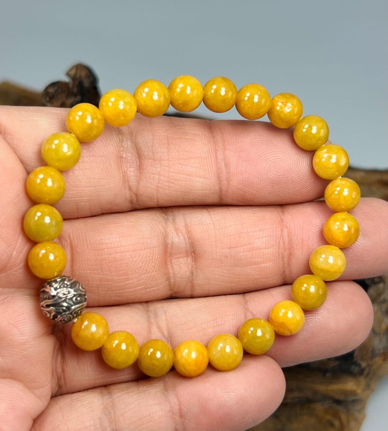 Pode incluir: Uma pulseira de contas redondas amarelas. A pulseira tem uma conta prateada ornamentada. As contas s&atilde;o de uma cor amarela vibrante. A pulseira &eacute; mostrada na m&atilde;o de uma pessoa.