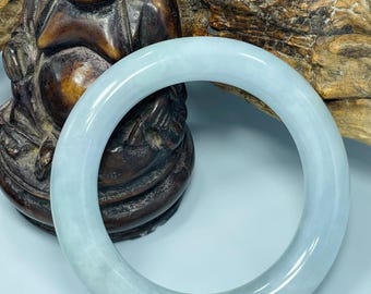 May include: A light blue jade bangle bracelet. The bracelet has a smooth, polished surface with subtle variations in color, ranging from pale blue to hints of green. The circular design is a classic jewelry style.