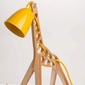 May include: A whimsical table lamp shaped like a giraffe. The lamp features a yellow lampshade and a wooden frame with cut-out details. A yellow cord and a black switch complete the design. The lamp is a decorative lighting fixture.